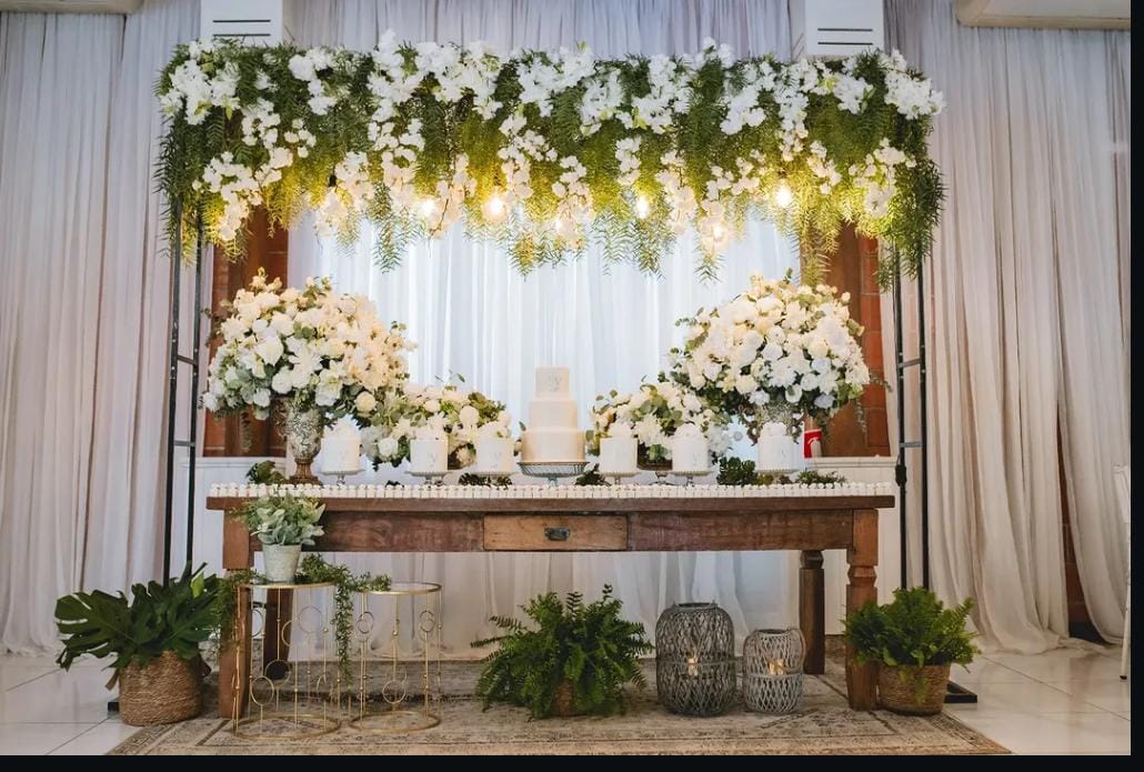 Mesa do bolo rústica com painel de florais brancos e folhagens